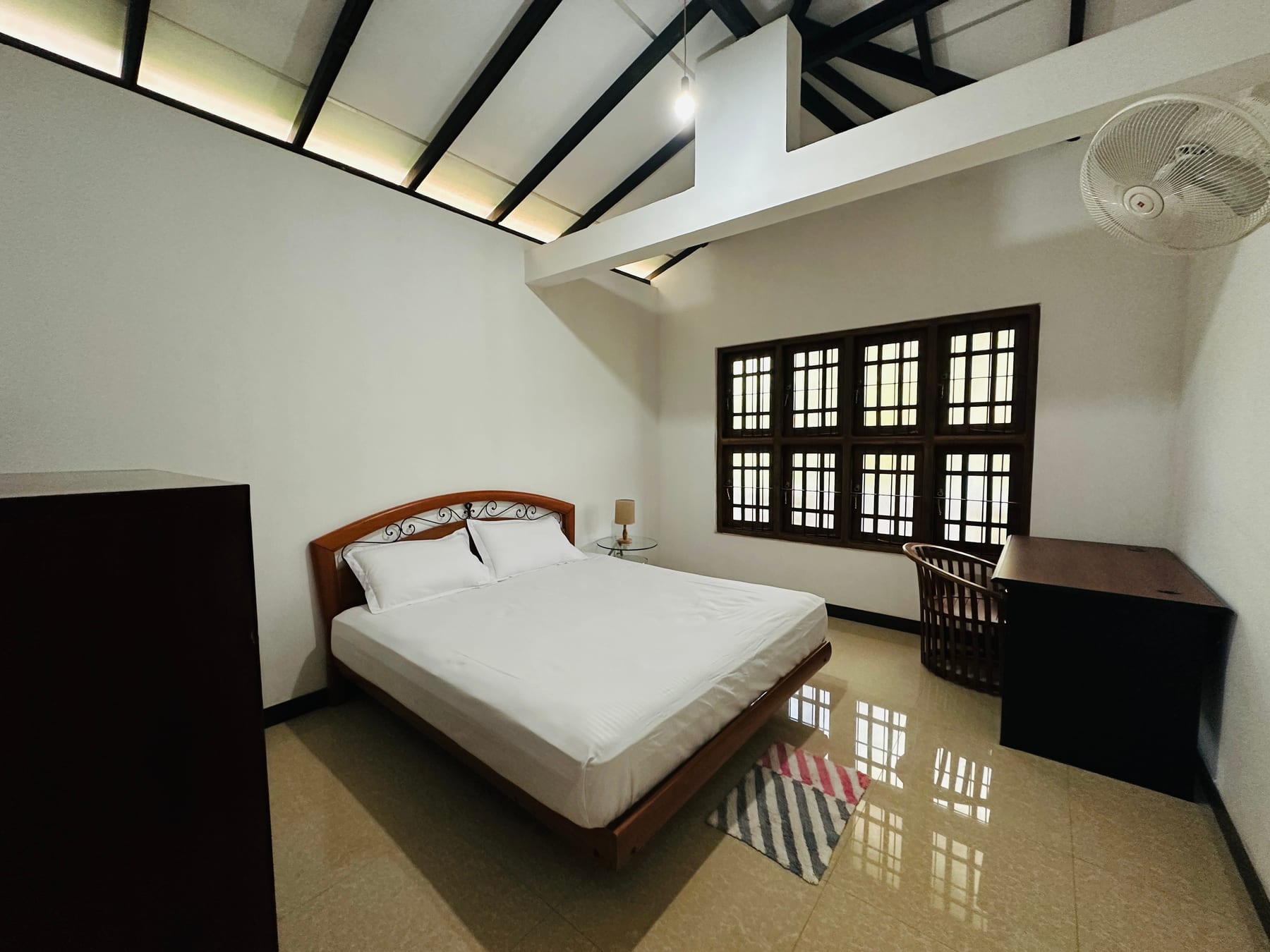 A bright bedroom with a timber bed and high ceiling